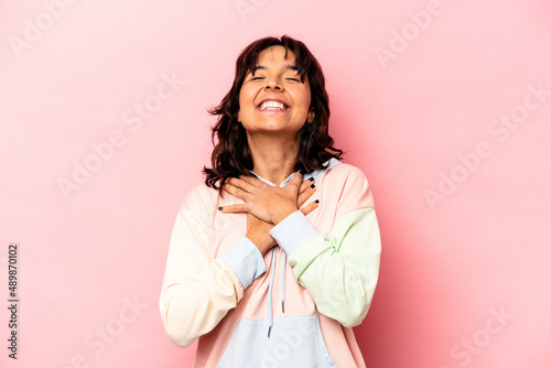 Young hispanic woman isolated on pink background laughs out loudly keeping hand on chest. © Asier