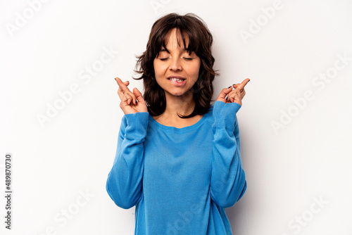 Young hispanic woman isolated on white background crossing fingers for having luck © Asier