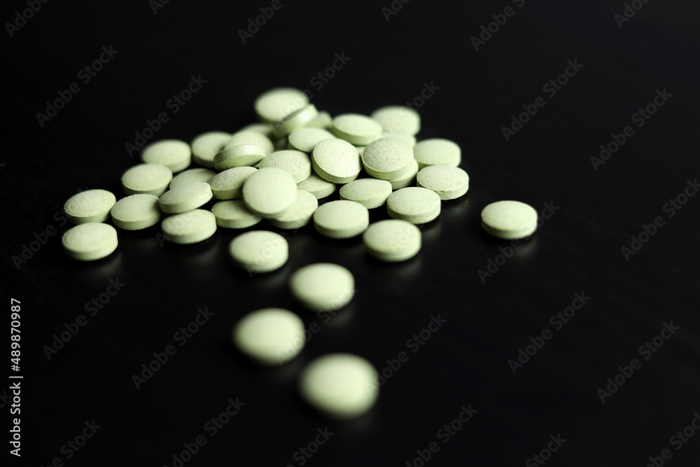 Green pills scattered on a dark wooden table. Herbal medicines, superfood for health Green pills scattered on a dark wooden table. Herbal medicines, superfood for health