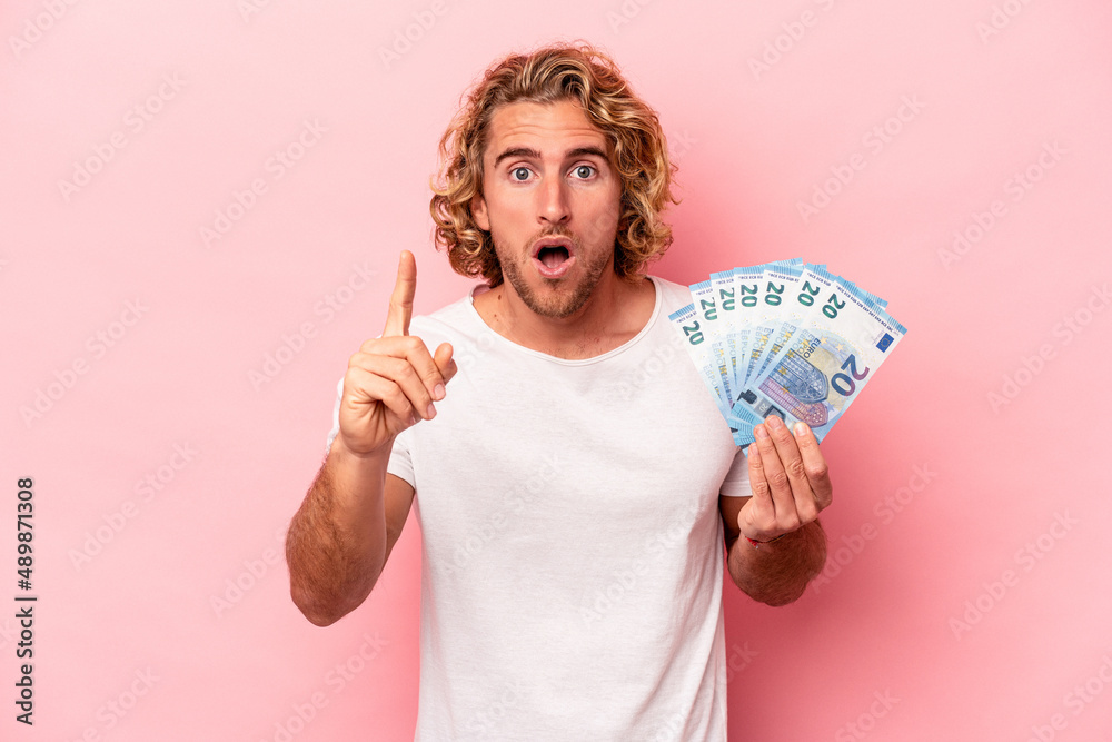 Young caucasian man holding banknotes isolated on pink background having an idea, inspiration concept. - obrazy, fototapety, plakaty 