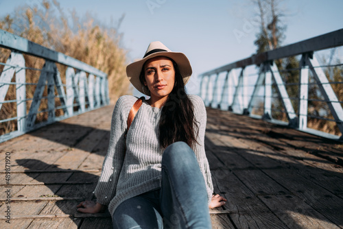 Portrait of a Hispanic woman with hat and backpack sitting at the entrance of a dock