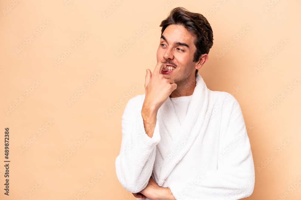 Young caucasian man wearing a bathrobe isolated on beige background relaxed thinking about something looking at a copy space. Young caucasian man wearing a bathrobe isolated on beige background relaxed thinking about something looking at a copy space.