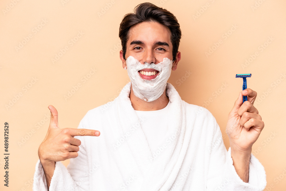 Young caucasian man shaving his beard isolated on beige background person pointing by hand to a shirt copy space, proud and confident Young caucasian man shaving his beard isolated on beige background person pointing by hand to a shirt copy space, proud and confident