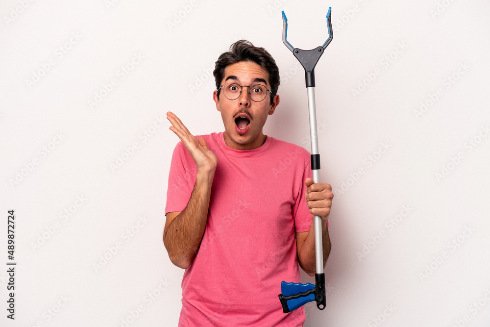 Young caucasian man holding a garbage collector isolated on white background surprised and shocked. Young caucasian man holding a garbage collector isolated on white background surprised and shocked.