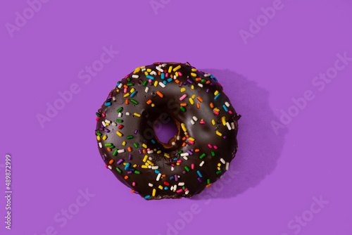 Donut covered with chocolate and sprinkles on a purple surface.