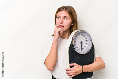 Young English woman holding a scale isolated on white background relaxed thinking about something looking at a copy space.