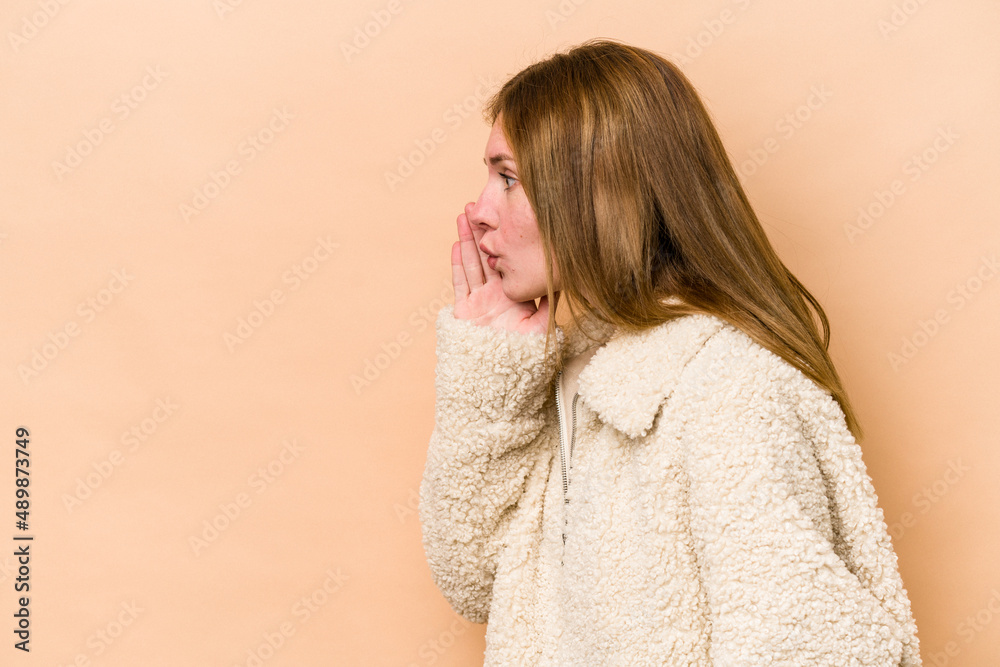 Young English woman isolated on beige background is saying a secret hot braking news and looking aside Young English woman isolated on beige background is saying a secret hot braking news and looking aside