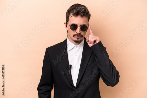 Young bodyguard caucasian man isolated on beige background pointing temple with finger, thinking, focused on a task.