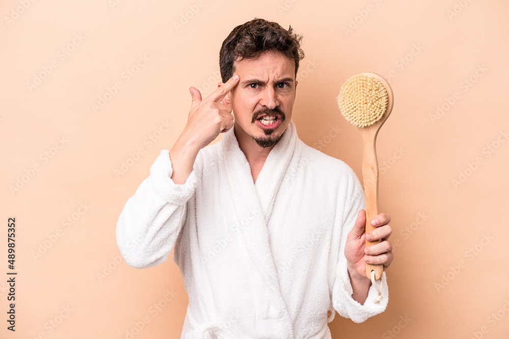 Young caucasian man holding back scratcher isolated on beige background showing a disappointment gesture with forefinger. Young caucasian man holding back scratcher isolated on beige background showing a disappointment gesture with forefinger.