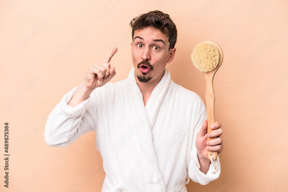 Young caucasian man holding back scratcher isolated on beige background having an idea, inspiration concept. Young caucasian man holding back scratcher isolated on beige background having an idea, inspiration concept.