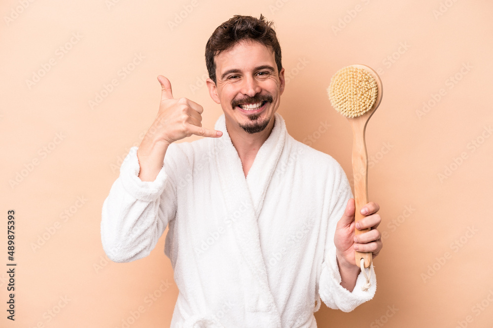 Young caucasian man holding back scratcher isolated on beige background showing a mobile phone call gesture with fingers. Young caucasian man holding back scratcher isolated on beige background showing a mobile phone call gesture with fingers.