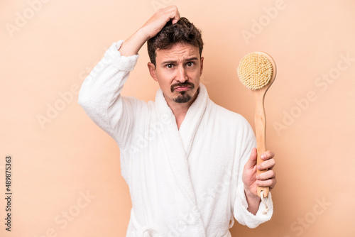 Young caucasian man holding back scratcher isolated on beige background being shocked, she has remembered important meeting.