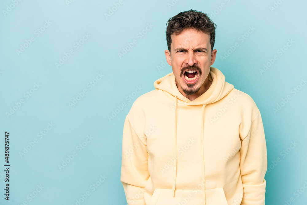 Young caucasian man isolated on blue background shouting very angry, rage concept, frustrated. Young caucasian man isolated on blue background shouting very angry, rage concept, frustrated.