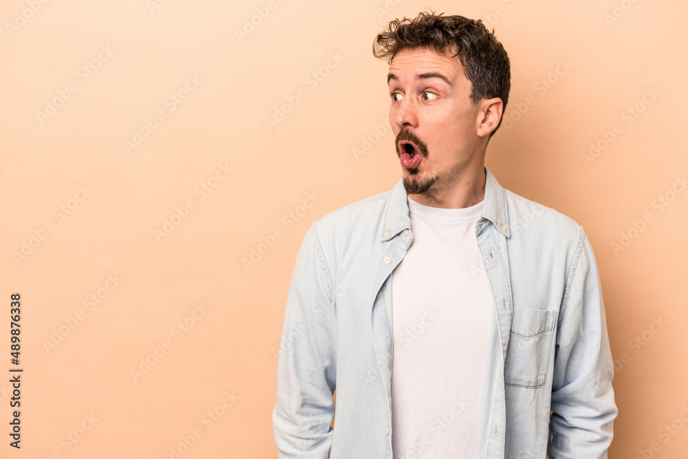 Young caucasian man isolated on beige background being shocked because of something she has seen.