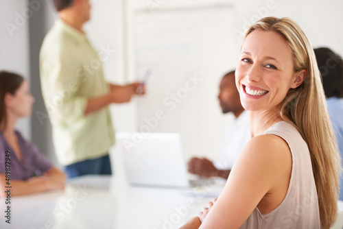 Content in her career and team. A smiling businesswoman looking at you while in a team meeting.