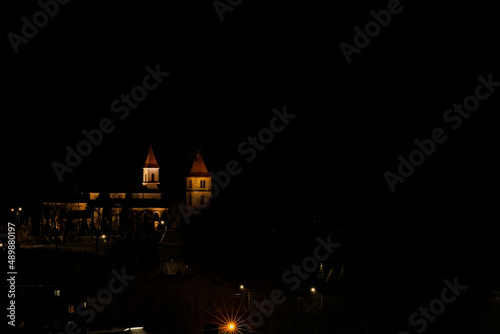 Kościół , pod wezwaniem św. Władysława , w Kunowie ( woj Świętokrzyskie ) , nocą , oświetlony , na tle świateł miasta .