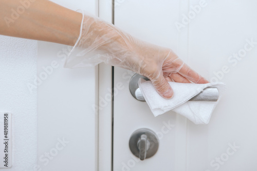 Cleaning door handles with wet wipe and white gloves. Woman hand using towel for cleaning home room door link. Sanitize surfaces prevention in hospital and public spaces against corona virus