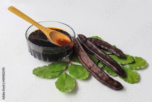 carob molasses in glass bowl and in wooden spoon and carob pods on rustic background, locust bean healthy food, Ceratonia siliqua ( harnup ) photo