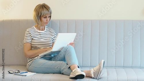 An elderly beautiful woman works at home at a laptop in the home office. The concept of remote work in old age.