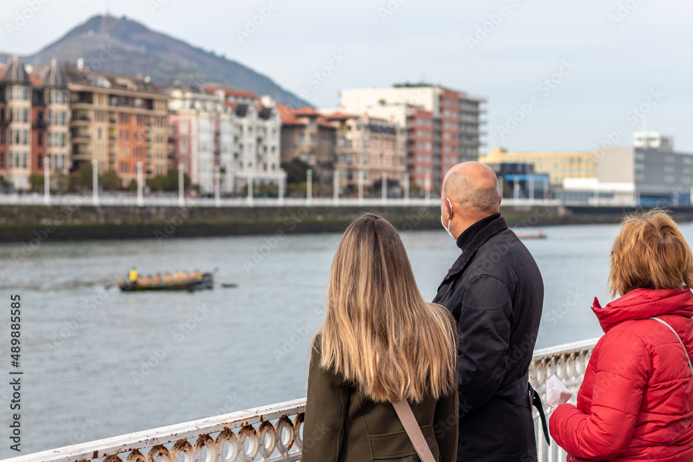 Family of three walking near a river while watching people rowing Family of three walking near a river while watching people rowing