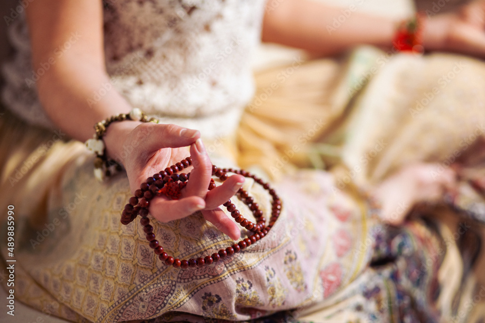 Fototapeta premium Woman at meditate place in lotus position using Mudra, hand close up, strands of beads used for keeping count during mantra meditations