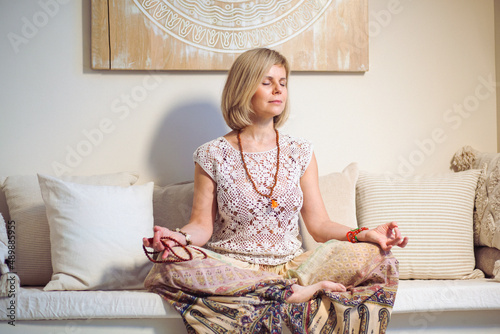 The concept of zen, peace, balance. A woman sits on a sofa and meditates  using Mudra, keeping her eyes closed and legs crossed