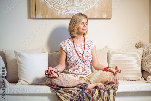 The concept of zen, peace, balance. A woman sits on a sofa and meditates  using Mudra, keeping her eyes closed and legs crossed