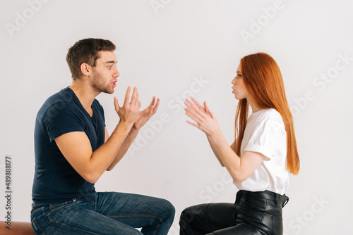 Studio shot of displeased young couple quarreling, actively gesturing with hands, talking and shouting at each other on white isolated background. Concept of relationship crisis.