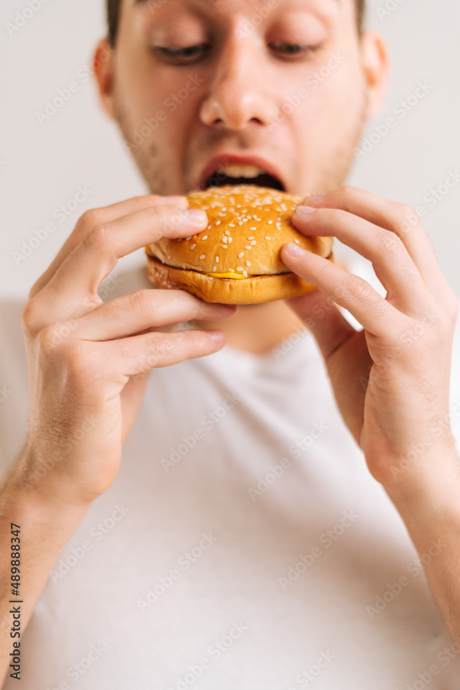 Vertical cropped shot of handsome young man with enjoying eating delicious burger on white isolated background. Close-up studio portrait of happy handsome male holding tasty unhealthy hamburger. Vertical cropped shot of handsome young man with enjoying eating delicious burger on white isolated background. Close-up studio portrait of happy handsome male holding tasty unhealthy hamburger.