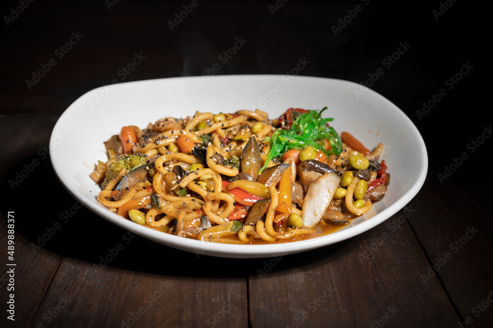 Asian vegetarian food udon noodles with shiitake mushrooms, sesame and pepper close-up on a plate on the wooden table. High quality photo