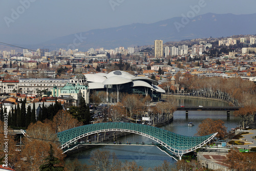 Aerial view of the Bridge of Peace, a pedestrian bridge made of steel and glass with a curvy design, over the Kura Mtkvari river in Tbilisi, Georgia. The Public Service Hall is seen in the background.