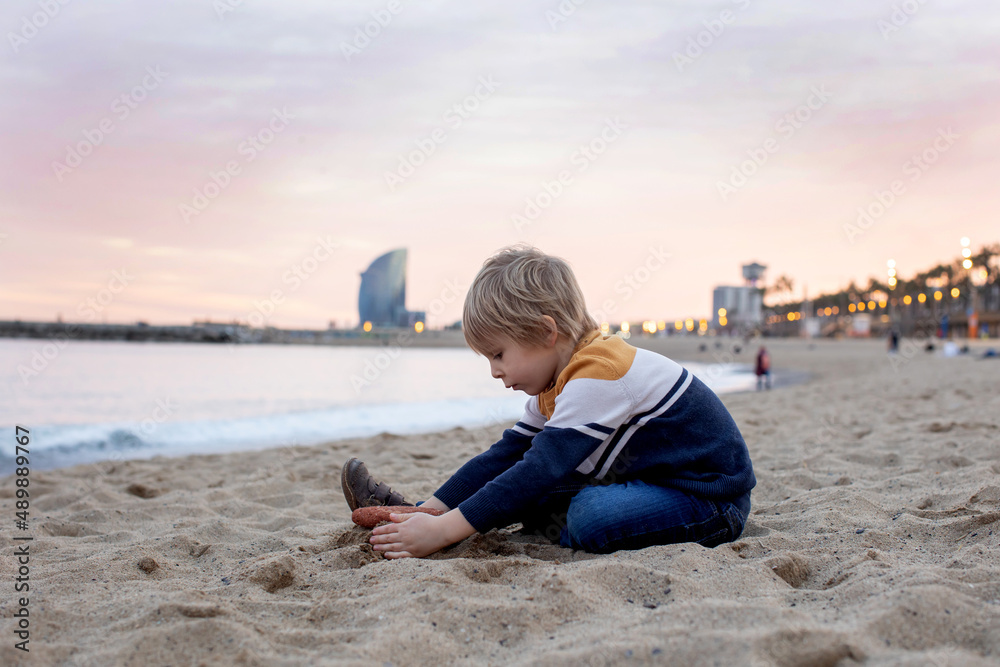 Cute little child, toddler boy, playing on the beach in Barcelona city, family travel with kids