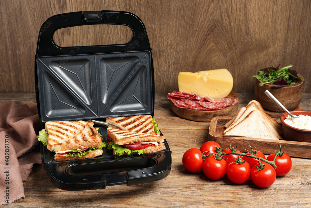 Ταπετσαρία Modern grill maker with sandwiches and different products on wooden table