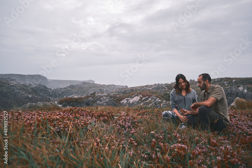 Happy young loving couple sitting in a meadow of flowers and plants, touching the flowers, green and military scout style