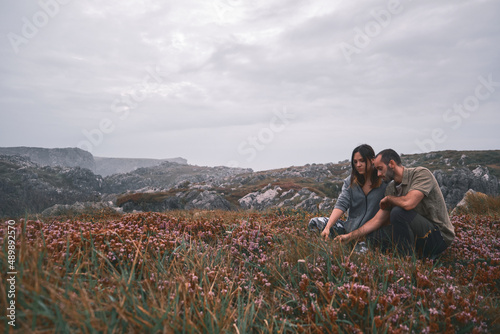 Happy young loving couple sitting in a meadow of flowers and plants, touching the flowers, green and military scout style