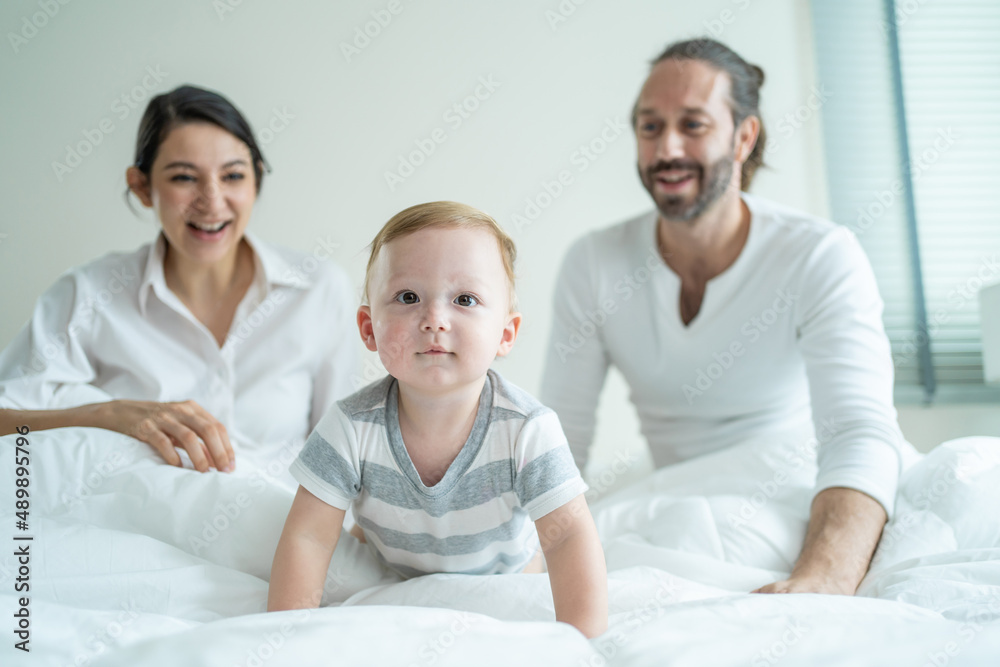Caucasian loving parents play with baby boy child on bed in bedroom. Caucasian loving parents play with baby boy child on bed in bedroom.