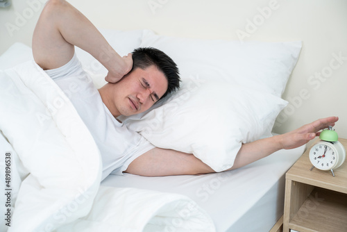 Asian attractive young man turn off alarm clock ringing in the morning. 