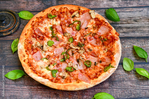  Close up of   classic  italian pizza   with ham. Fresh basil,tomato sauce ,mozzarella cheese , mushrooms and  green peppers #489896540