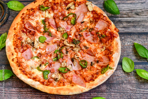  Close up of classic italian pizza with ham. Fresh basil,tomato sauce ,mozzarella cheese , mushrooms and green peppers