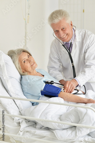 Portrait of senior woman portrait in hospital with caring doctor measuring pressure