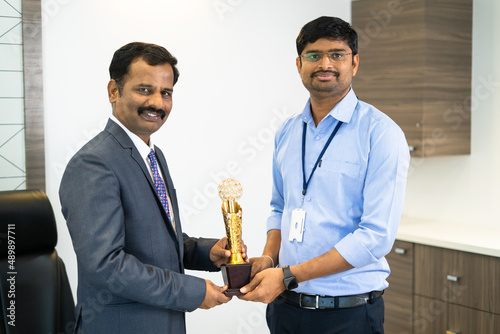 Fotografi Young corporate employee receiving trophy from boss in office - concept of best