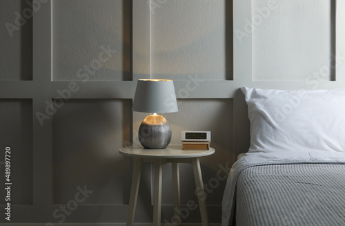 Stylish lamp, alarm clock and book on bedside table indoors. Bedroom interior elements photo