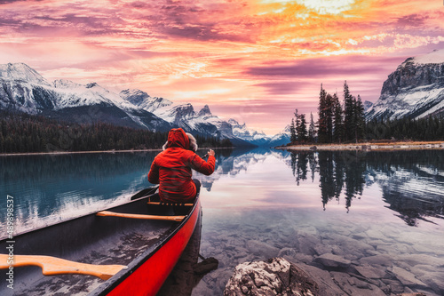 Male traveler in winter coat rowing a red canoe in Spirit Island on Maligne Lake at the sunset