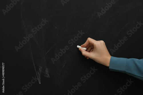 Woman with white chalk near blackboard, closeup. Space for text