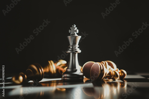Obraz na plátne Silver chess king standing on a board surrounded by gold chess pieces