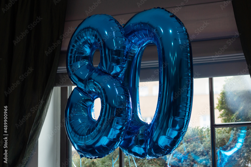 80th birthday balloons are mounted by a window in a restaurant before a birthday party.