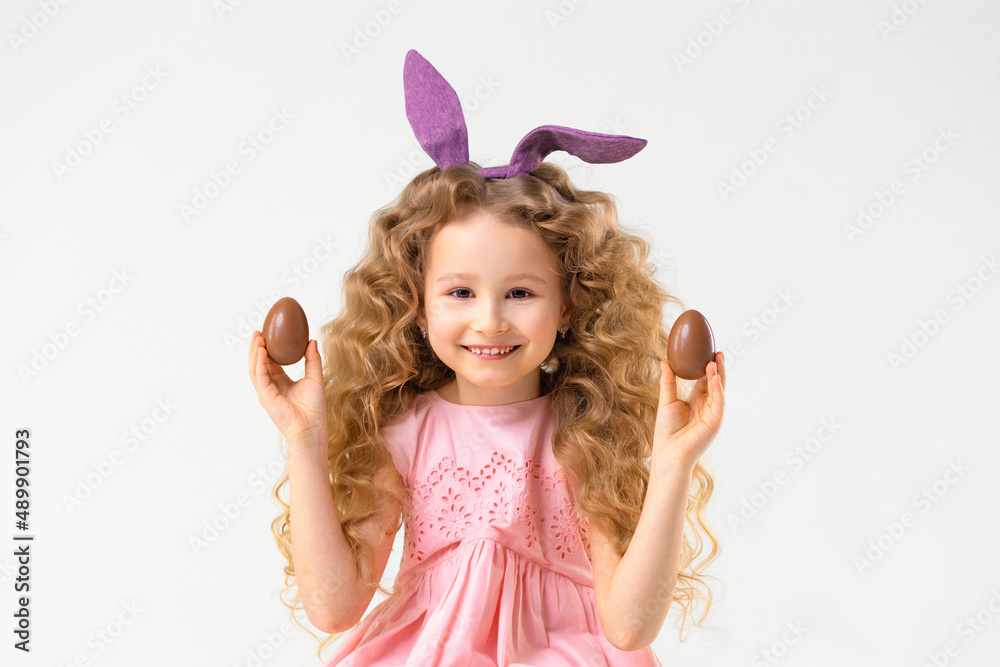 Happy holiday easter kids. Smiling cute little beautiful girl with rabbit hare bunny ears playing with chocolate eggs