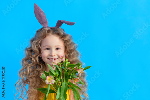 Happy holiday easter kids. cute little beautiful smiling girl with rabbit hare bunny ears, spring flowers on blue background, banner, copy space, tex