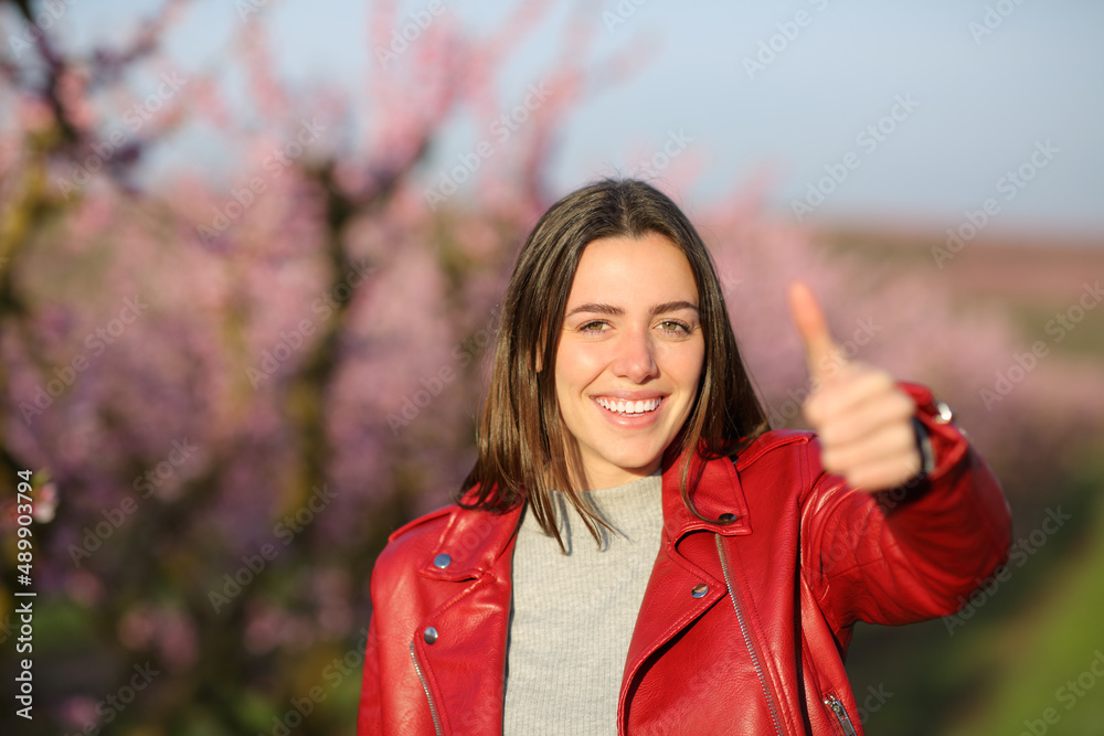 Happy woman in red gesturing thumb up in a field