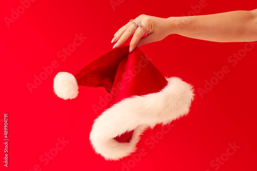 Close Up Studio Shot Of Woman Holding Christmas Santa Hat Against Red Background